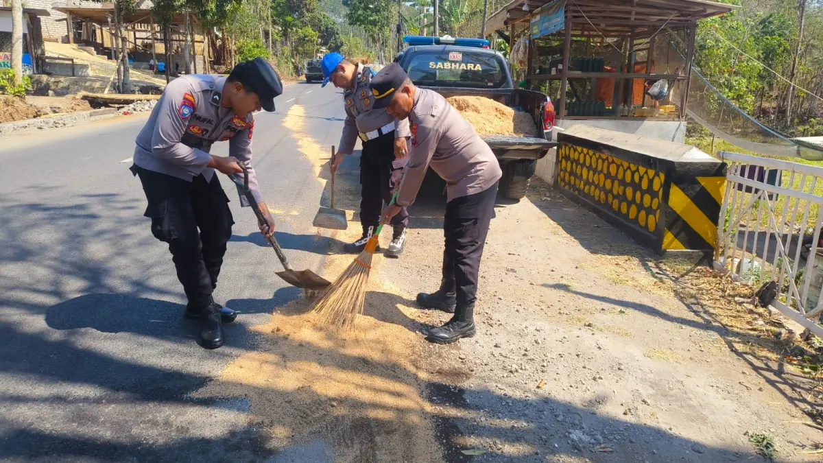 DIBERSIHKAN: Anggota Polsek Wringin membersihkan tumpahan solar yang ada di jalan raya, menggunakan alat seadanya, kemarin. (ILHAM WAHYUDI/RADAR IJEN)