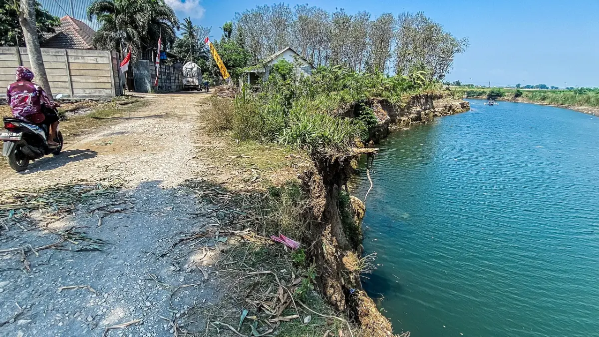 JALAN TEPI SUNGAI: Kondisi jalan di Desa Lojejer, Kecamatan Wuluhan terus terkikis. Bahkan, membuat rumah dan warung di sekitarnya was-was. (JUMAI/RADAR JEMBER)