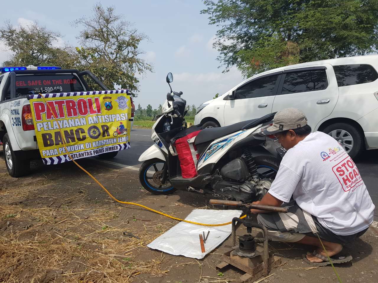 OPERASI BAN BOCOR: Petugas tambal ban keliling yang disiapkan oleh Satlantas Polres Jember sedang menambal ban motor milik pemudik yang melintas di jalur utama Jember-Lumajang.