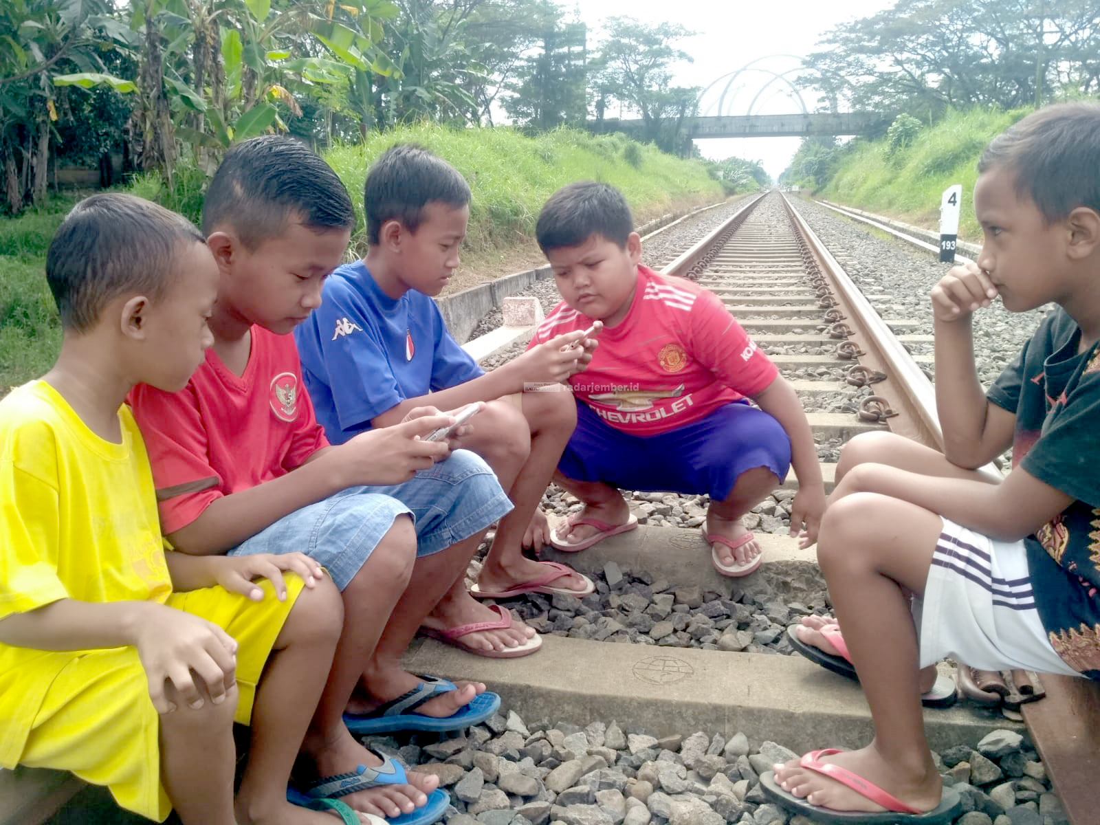 Lima anak kecil tampak asyik di rel kereta api di Jalan Gajah Mada, Kecamatan Kaliwates.