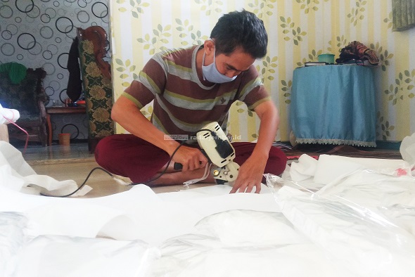 BANYAK PESANAN: Sugiyono, 49, pemilik salah satu konveksi di Jalan Melati, Kelurahan Jember Kidul, Kecamatan Kaliwates, saat memotong kain untuk baju alat pelindung diri (APD).