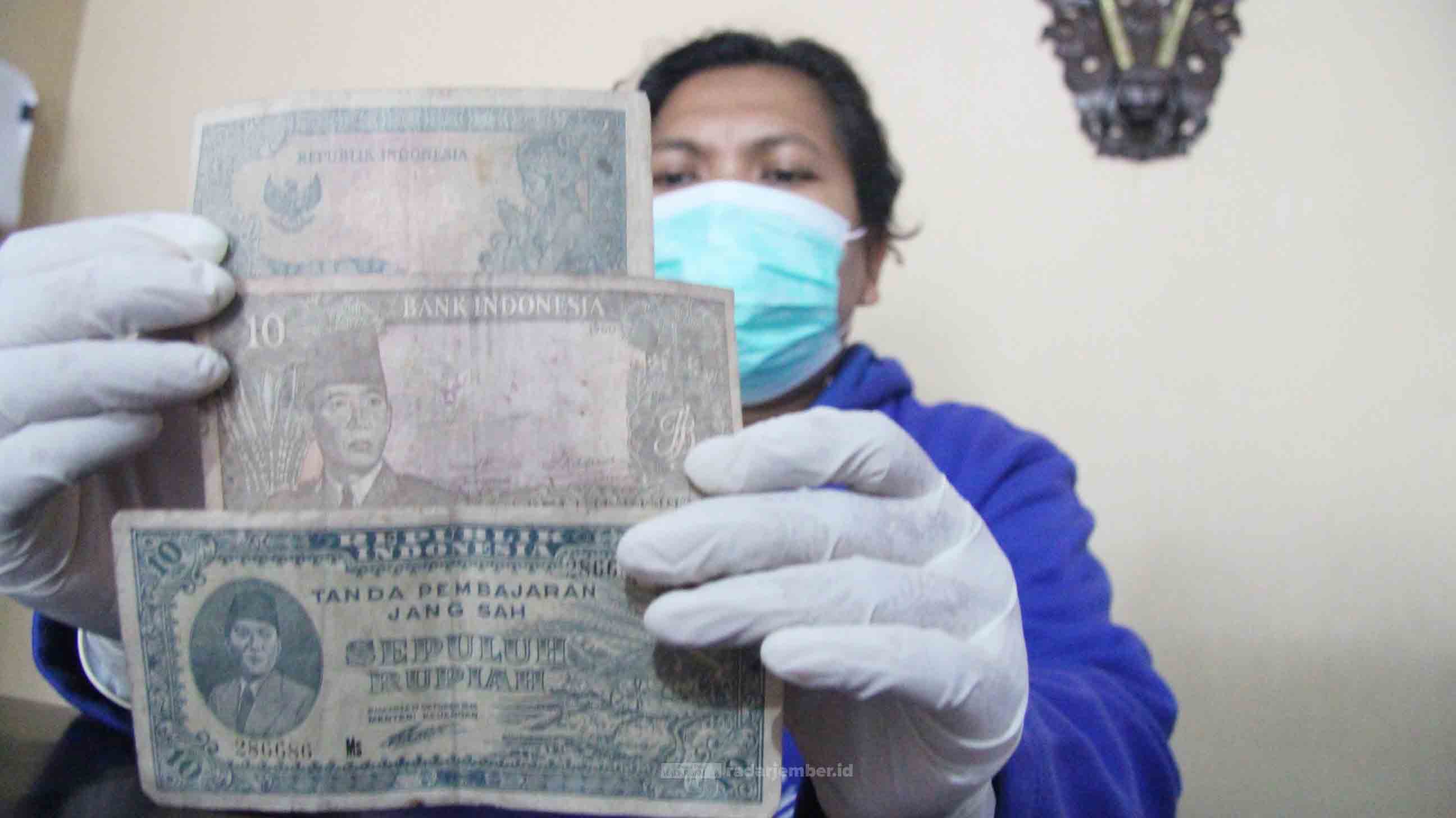 TUNJUKKAN: Salah satu pegawai Dinas Pariwisata dan Kebudayaan (Disparbud) Lumajang saat menunjukkan tambahan koleksi uang kertas yang dikeluarkan tahun 1945 silam beserta beberapa koin yang digunakan untuk transaksi dahulu kala.   