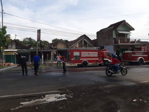 DIBERSIHKAN: Sejumlah petugas ketika membersihkan tumpahan solar di sekitar Pasar Induk Bondowoso. Akibat tumpahan tersebut, lima pemotor terjatuh.