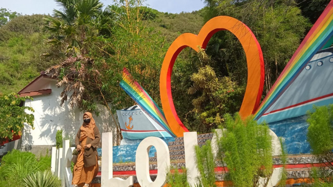 PENGUNJUNG: Chairunnisah Nurul Aini, wisatawan asal Lumajang, menikmati pemandangan dan mengambil foto di papan nama wisata Teluk Love.