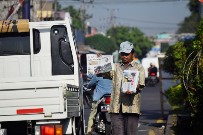 SANG PROMOTOR: Nur Hasan menunjukkan berita headline Jawa Pos Radar Jember kepada pengendara mobil yang melintas di simpang empat Mangli, Rabu (13/7).