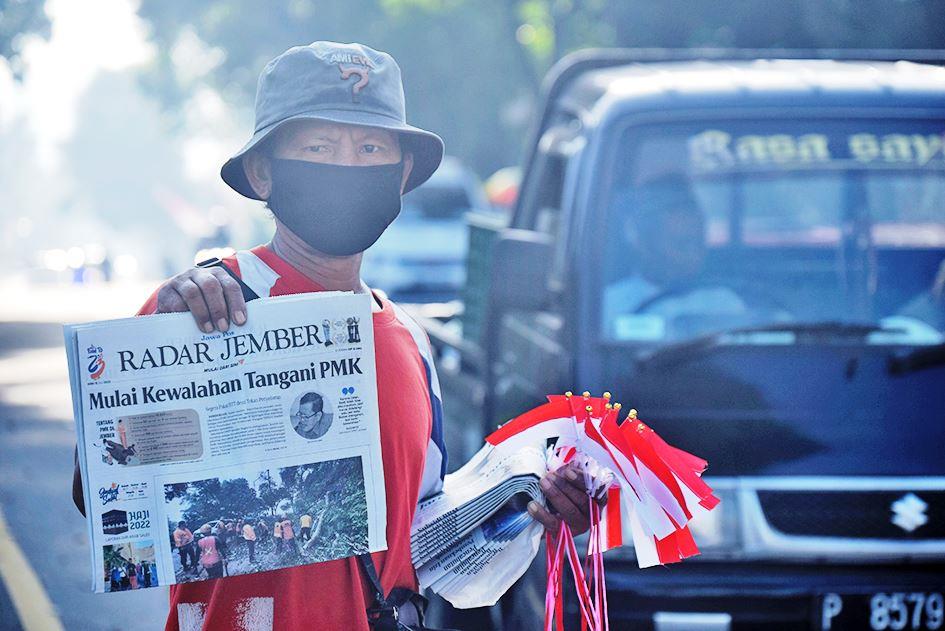 PANTANG MENYERAH: Azis Kuswoyo, loper yang mangkal di perempatan Argopuro, menyapa pengendara sambil memperlihatkan berita headline koran Radar Jember.