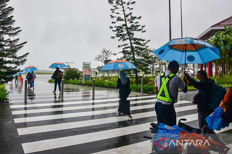 Caption Foto :  Arsip Foto. Seorang petugas bandara (kanan) memberikan payung kepada calon penumpang yang hendak menuju ke pesawat saat hujan turun di kompleks Bandara Pattimura, Kota Ambon, Maluku, Senin (11/7/2022).