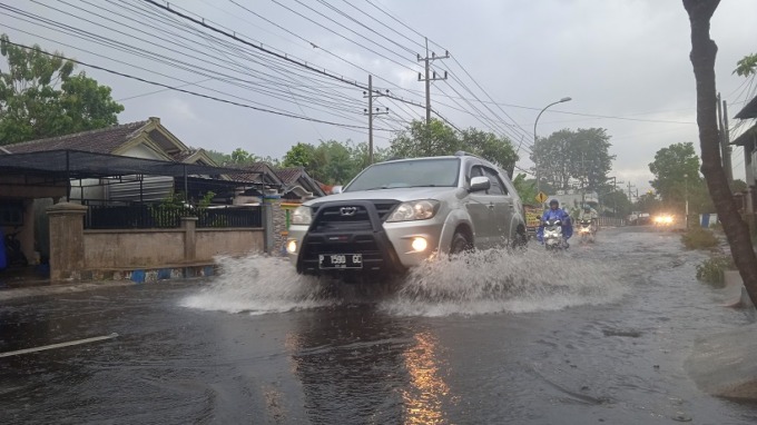 HATI-HATI: Pengendara saat melintasi genangan air di Jalan Aip Mugiman, Bondowoso. Drainase tersumbat mengakibatkan air memenuhi jalan hingga setinggi lutut.