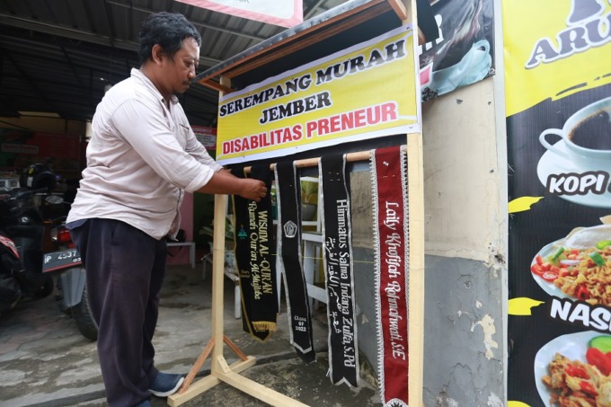DIJUAL: Udin merapikan selempang yang dijajakan di pinggir Jalan Bengawan Solo, Kelurahan/Kecamatan Sumbersari.   