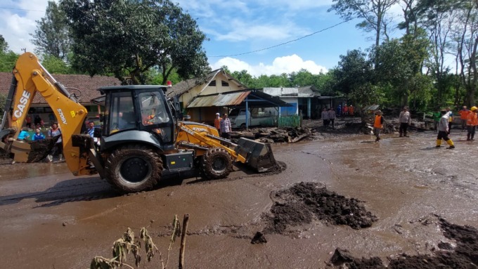 TERTUTUP LUMPUR: Personel kepolisian bersama-sama relawan dan warga membersihkan Jalan Raya Ijen yang tertimbun lumpur akibat banjir bandang.