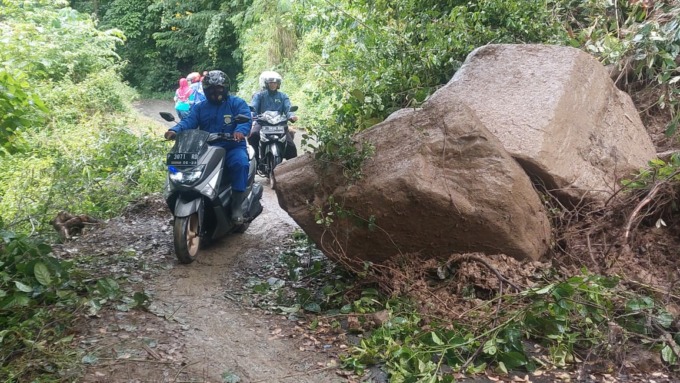 TERTUTUP BATU: Warga melewati batu besar yang menutup akses jalan di Desa Mulyorejo, Kecamatan Silo, Jember, Rabu (1/3). (Foto: Jumai/Radar Jember)