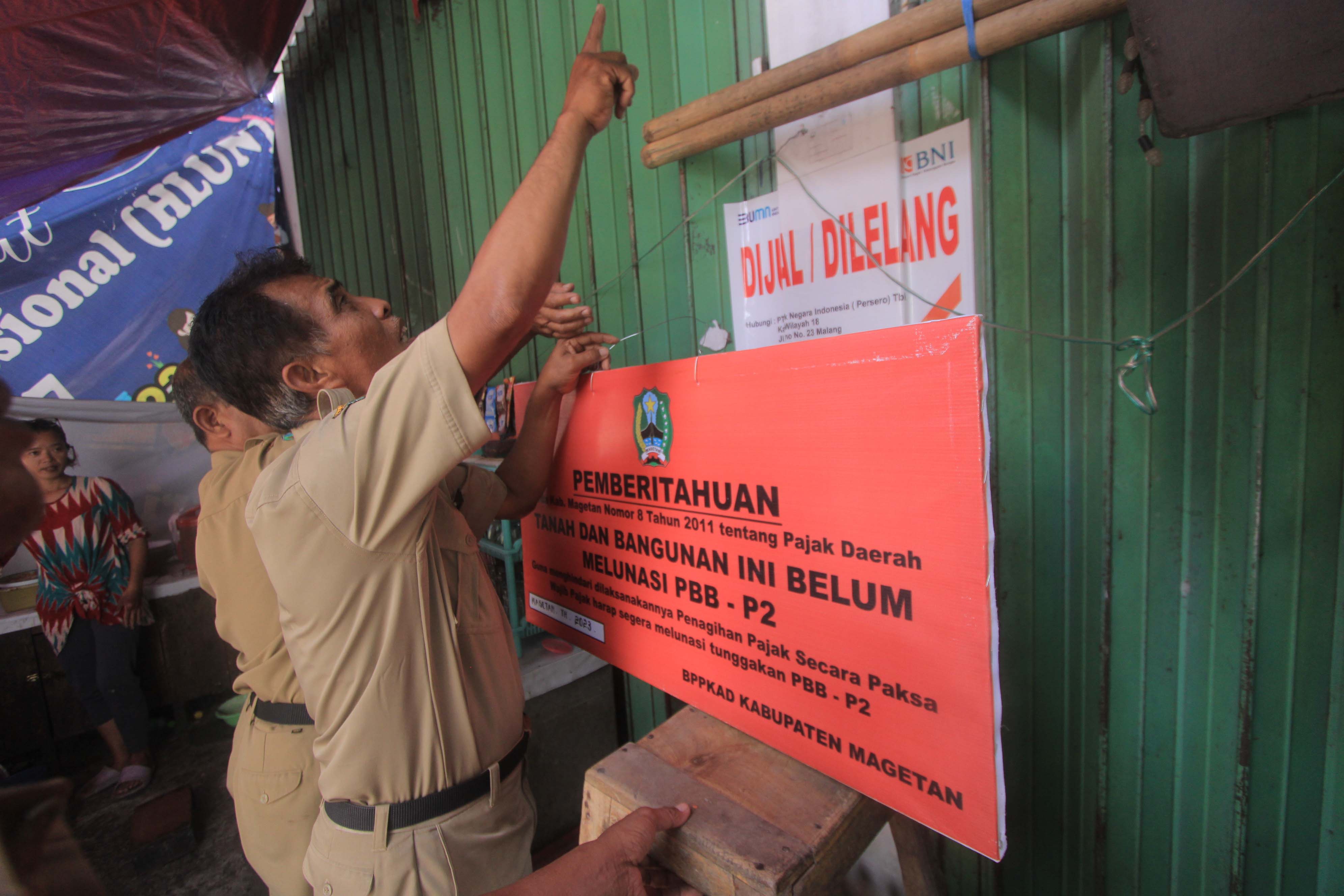 OBJEK PAJAK: Petugas BPPKAD memasang papan pemberitahuan terkait PBB-P2 di bangunan masuk Kelurahan Sukowinangun, Magetan, kemarin (6/11).&nbsp;(AJI PUTRA/JAWA POS RADAR MAGETAN)