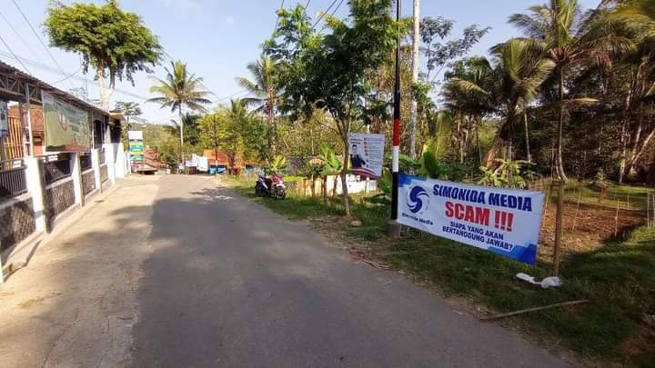 AWAS PENIPUAN: Warga memasang banner di wilayah Desa Kalikuning, Tulakan, yang berisi peringatan bahwa aplikasi Simonida Media scam alias penipuan.&nbsp;(ISTIMEWA)