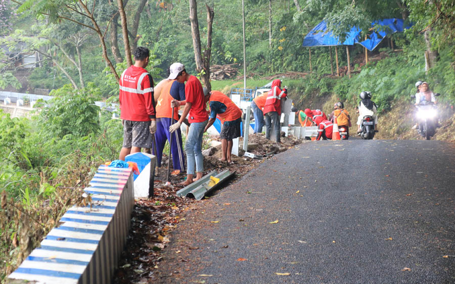 DITAMBAH: Sejumlah pekerja tengah memasang pembatas jalan di sisi selatan jalan lingkar Telaga Ngebel. (SUGENG DWI N./JAWA POS RADAR PONOROGO)