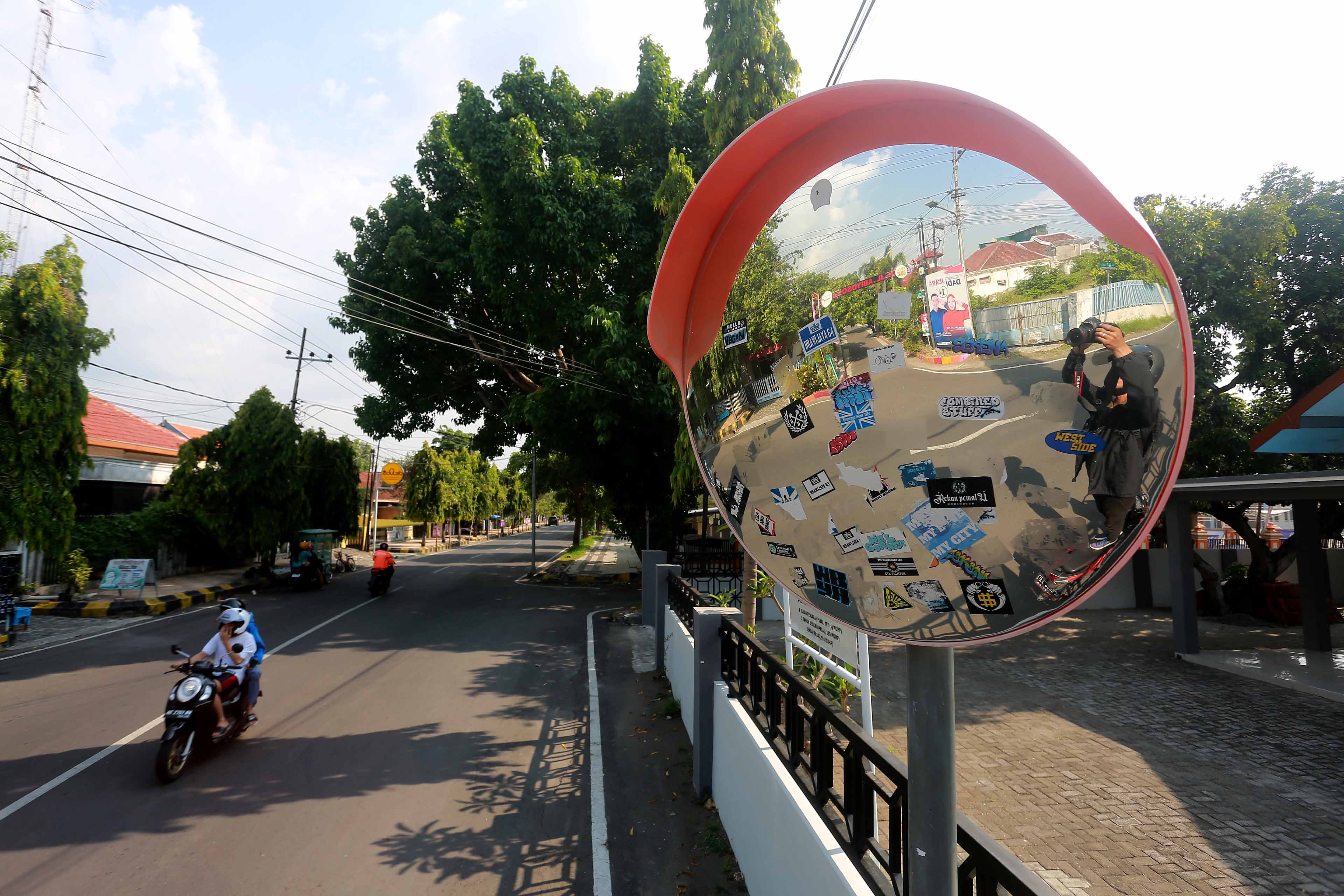 PENUH STIKER: Kaca cermin cembung lalin yang dipasang Dishub Kota Madiun di Jalan Parikesit menjadi korban vandalisme tangan jahil. (BAGAS BIMANTARA/RADAR MADIUN)
