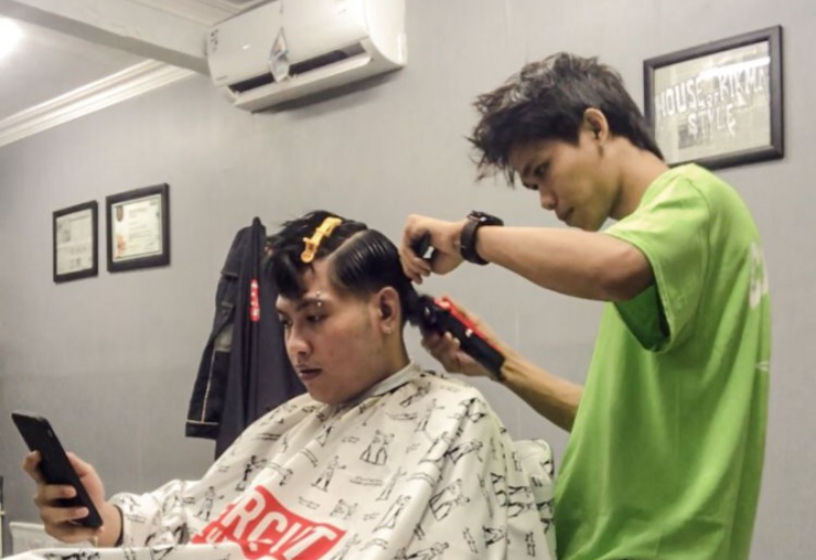 NGETREN: Ino Candra saat memotong rambut seorang customer. (SUCI OKTA/JAWA POS RADAR PACITAN)
