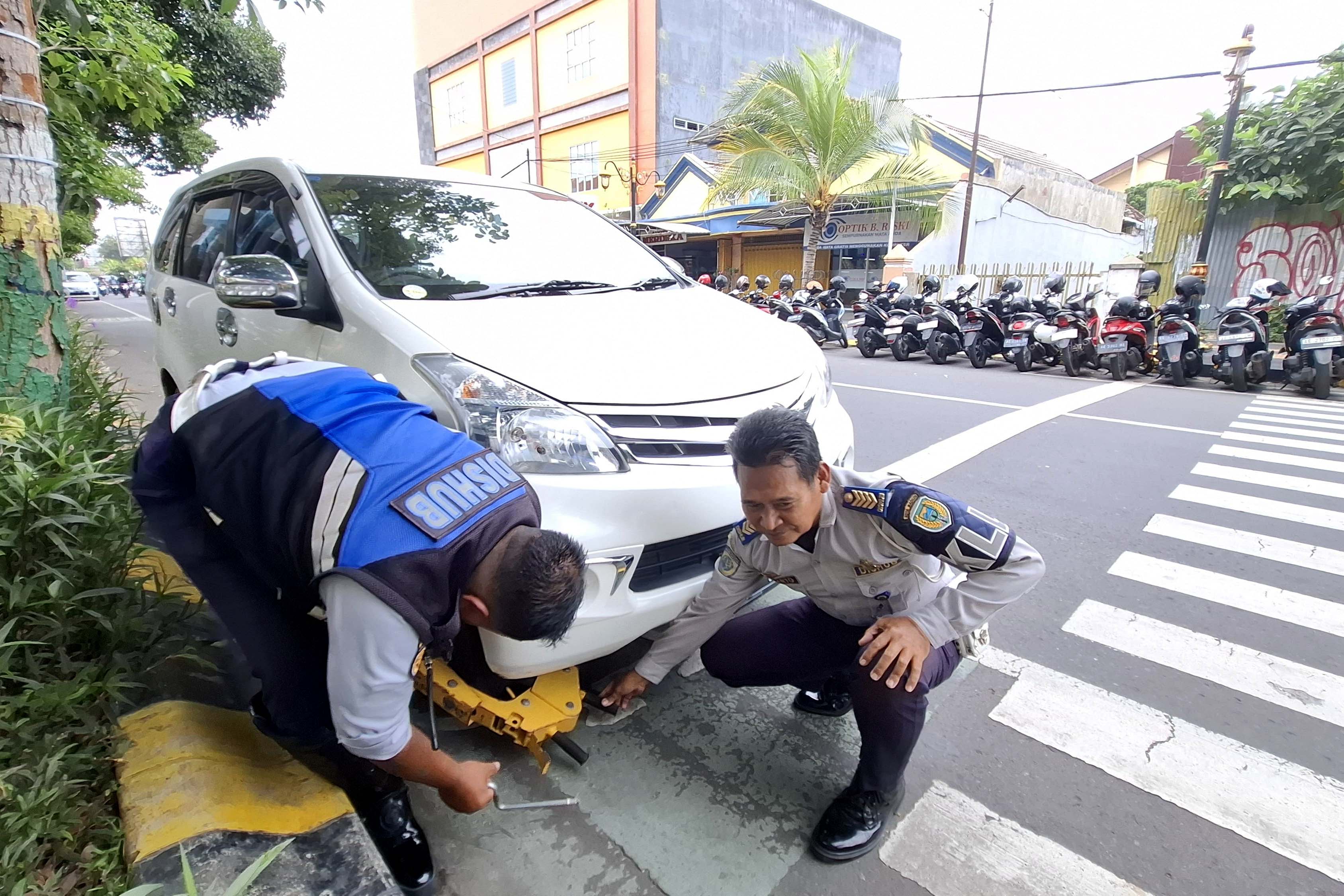 DIGRENDEL: Petugas Dishub Kota Madiun menggembok roda mobil yang terparkir di sisi kanan Jalan Dr Soetomo, Senin 3 Februari 2025.
