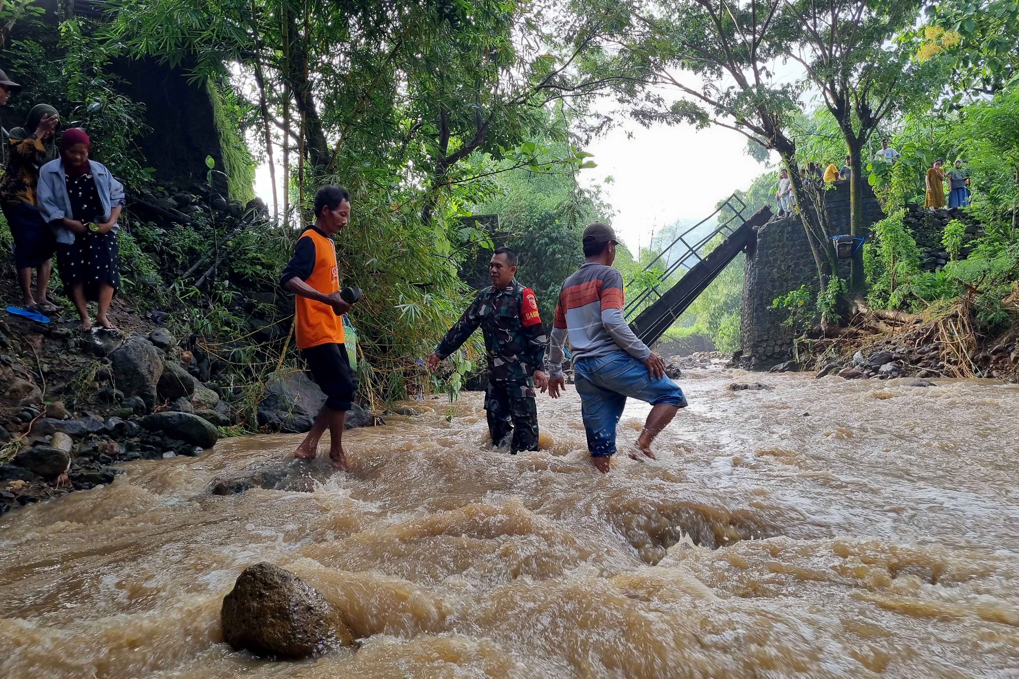 PERJUANGAN: Warga dibantu Babinsa Desa Munggu menyeberangi sungai lantaran jembatan putus diterjang banjir, Selasa 18 Maret 2025.
