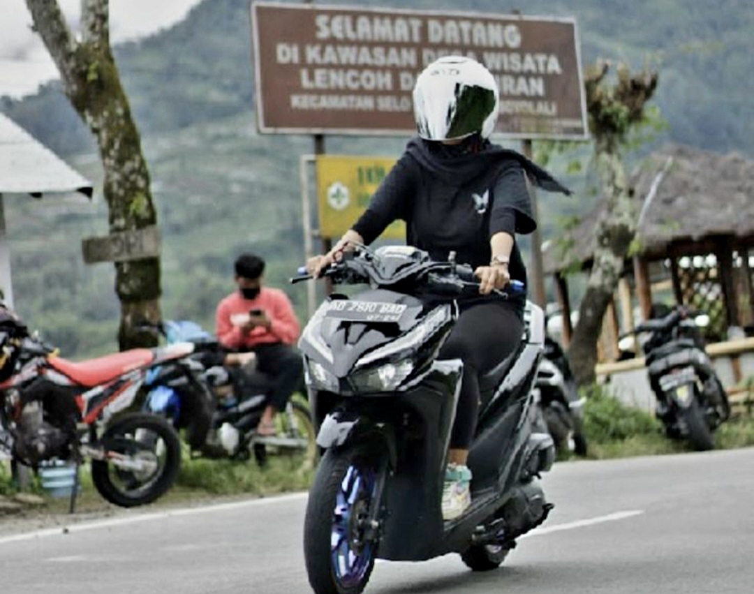 Ilustrasi cewek mengendarai motor matik di kawasan pegunungan.