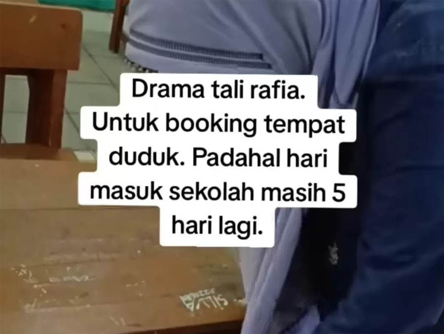 BOOKING TEMPAT : Seorang wali murid terlihat tengah mengikat tas anaknya dengan tali rapia pada bangku barisan paling depan di ruang kelas.