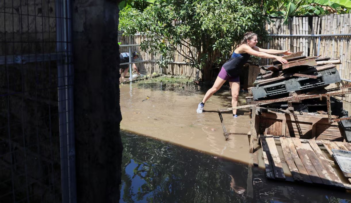 Seorang wisatawan mancanegara membersihkan material usai banjir yang menggenangi penginapannya di Bali.