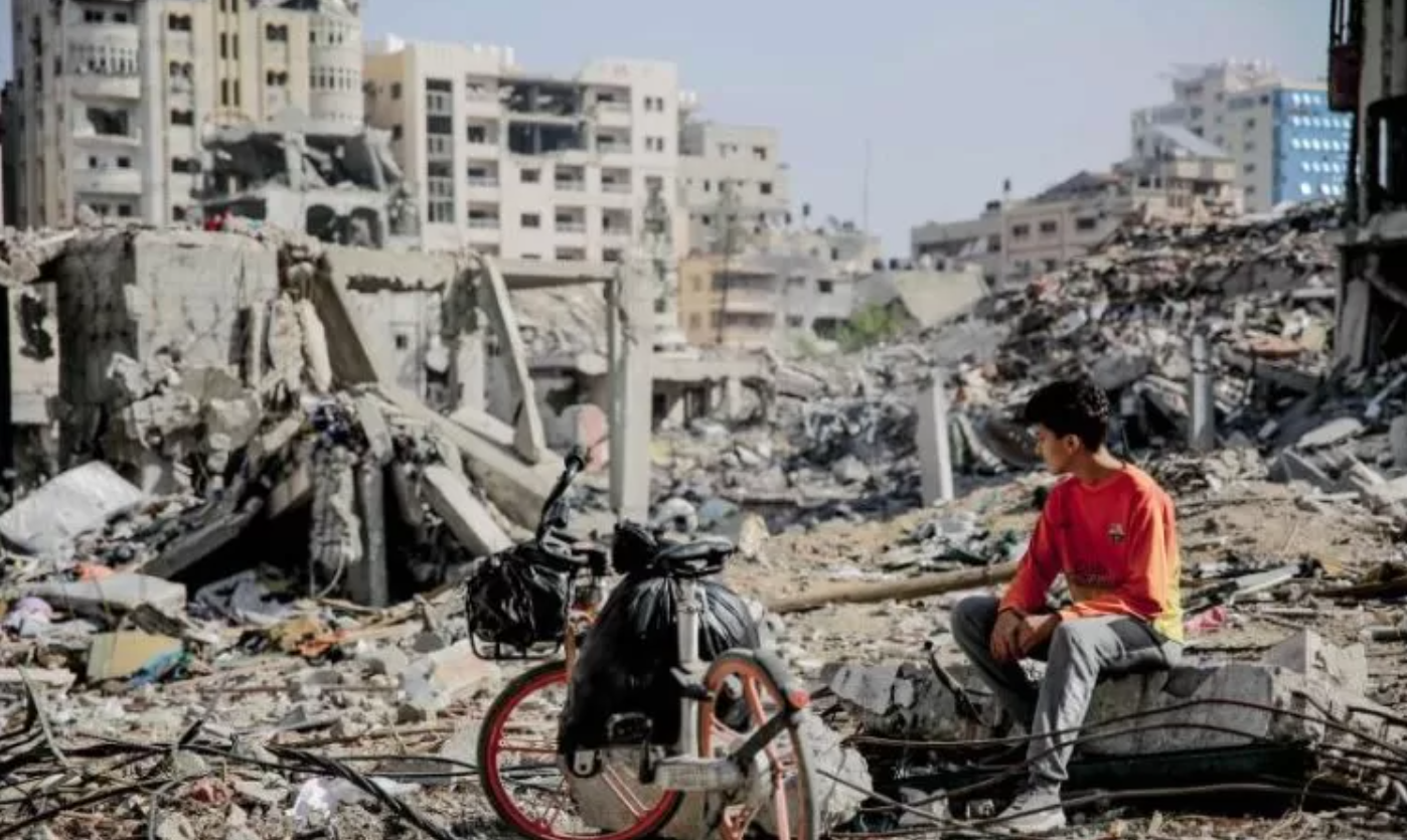 Seorang remaja Palestina duduk di samping sepedanya di tengah puing-puing bangunan yang hancur di Kota Gaza di jalur Gaza utara setelah berminggu-minggu pemboman Israel.