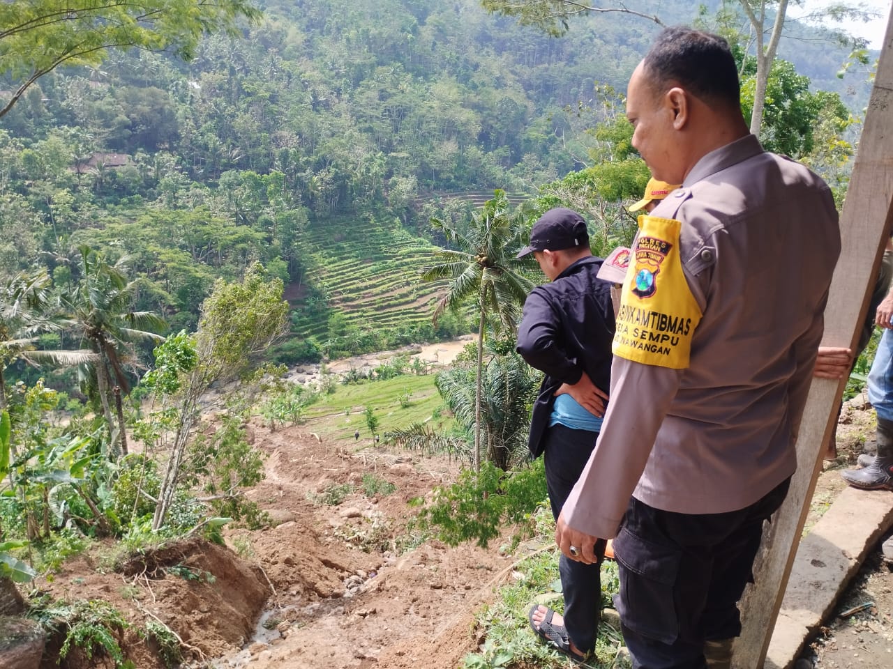 Polisi bersama warga bergotong royong membersihkan material longsor di belakang rumah Boyamin, Dusun Tanggung, Desa Sempu, Nawangan, Pacitan, usai hujan deras mengguyur wilayah tersebut.