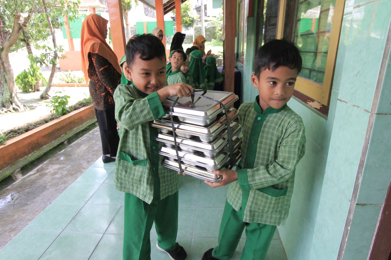 SEMANGAT: Siswa SDN Buluharjo 01 saling membantu membawa MBG ke kelas.