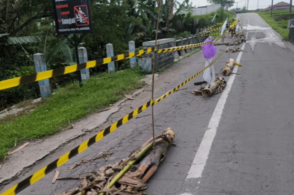 BAHAYA: DPUPR Ngawi memasang garis peringatan di jembatan ruas Jalan Gebung, Desa Pelang Kidul, Kedunggalar, setelah tanggul sisi barat ambrol akibat banjir, Selasa (17/2). ASEP SYAEFUL/RADAR NGAWI
