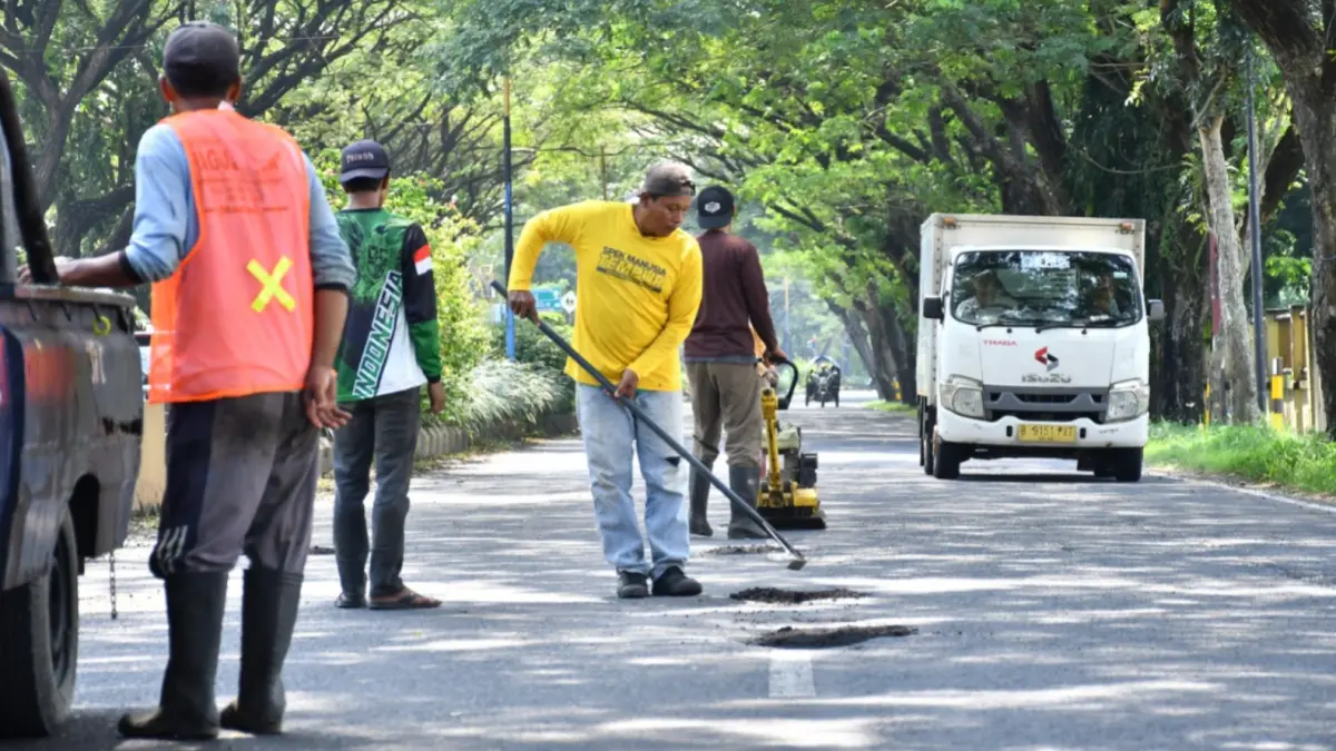 UPAYA DARURAT: Petugas DPUPR Kota Madiun saat melakukan tambal sulam jalan di salah satu sudut kota. Saat ini proyek pengaspalan besar masih tertunda akibat penyesuaian harga aspal dan BBM nonsubsidi. (FOTO: Radar Madiun)