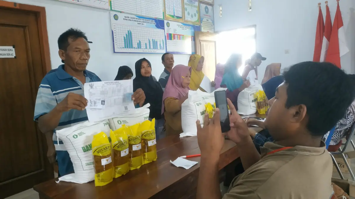 DAPAT MINYAK GORENG: Petugas membagikan minyak goreng minyak kita kepada warga penerima bantuan sejumlah 4 liter per orang. (SATRIO JATI WASKITO/RADAR MADIUN)
