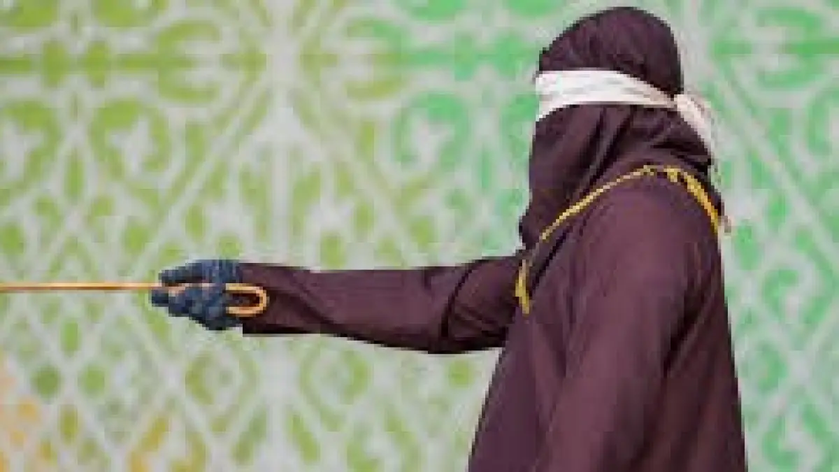 Seorang pejabat yang mengenakan jubah dan tudung bersiap untuk mencambuk seorang pelanggar hukum Syariah di Banda Aceh, Indonesia, pada hari Kamis. (The Guardian)