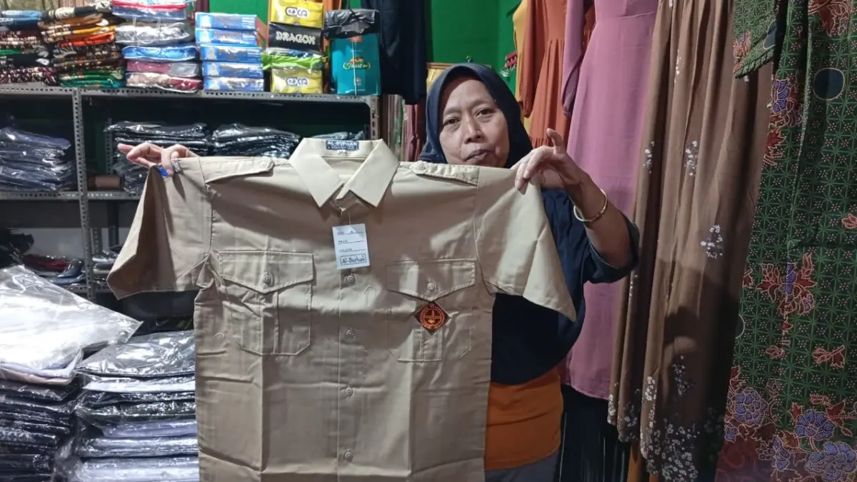 Pedagang seragam sekolah di Pasar Dolopo melayani pembeli. Memasuki tahun ajaran baru, penjualan justru lesu akibat persaingan dengan toko daring dan program seragam dari sekolah. Foto: Dian Rahayu/Radar Caruban.