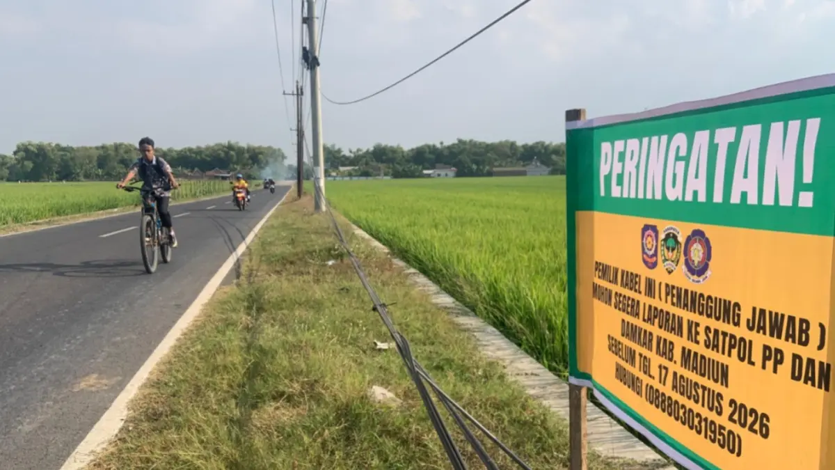 PERINGATAN: Satpol PP dan Damkar Kabupaten Madiun memasang papan peringatan di lokasi kabel semerawut di Desa Mojorayung.