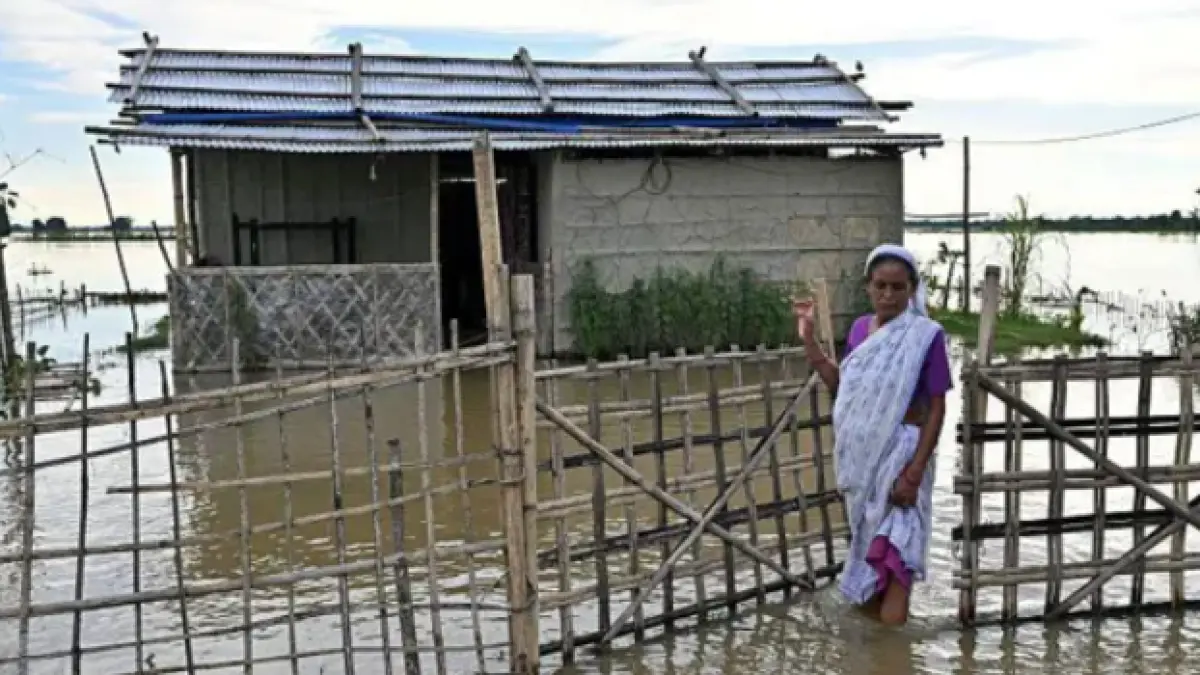 Seorang wanita berjalan menyeberangi genangan banjir di luar rumahnya yang terendam banjir di sebuah desa di Sivasagar, Assam (BBC)