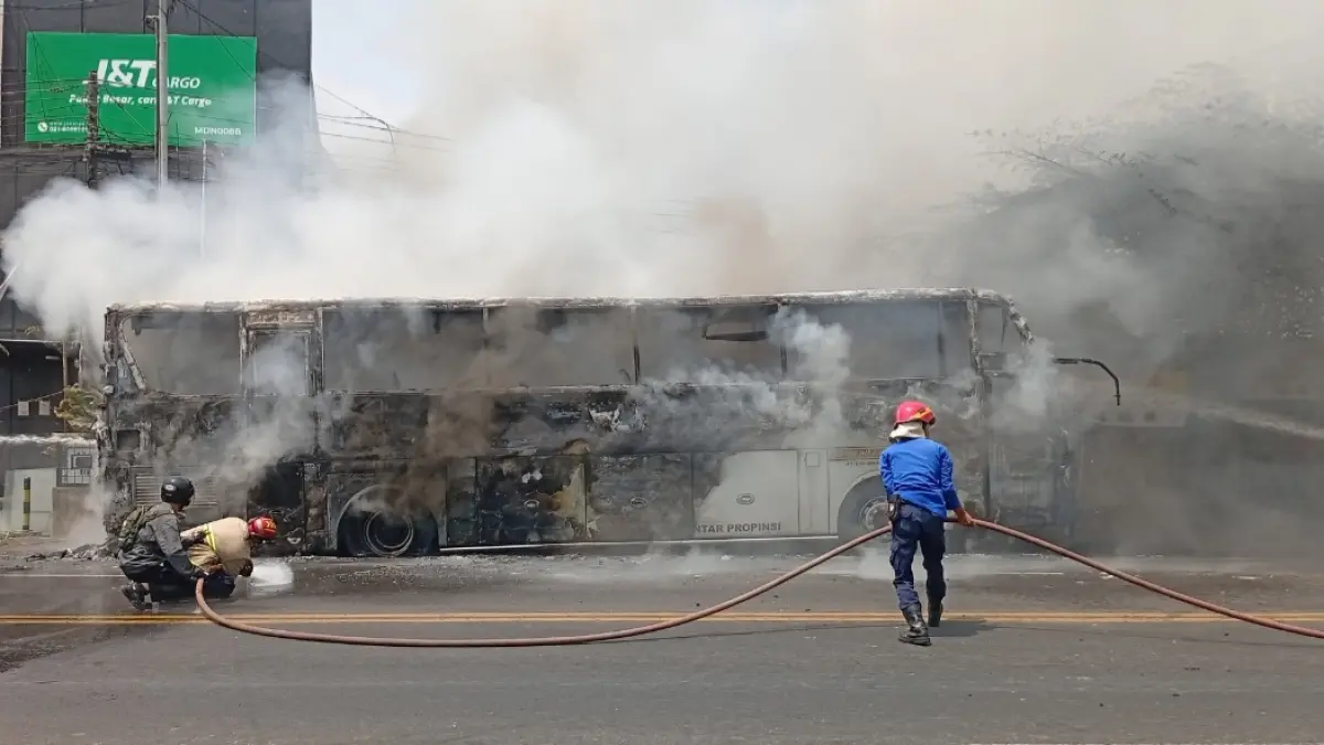 HANGUS: Petugas Damkar Kabupaten Madiun berusaha memadamkan Bus Eka yang terbakar hebat di Jalan Raya Nglames, Desa Tiron, Kecamatan Madiun, Sabtu (22/8) siang. (DIAN RAHAYU/RADAR MADIUN)