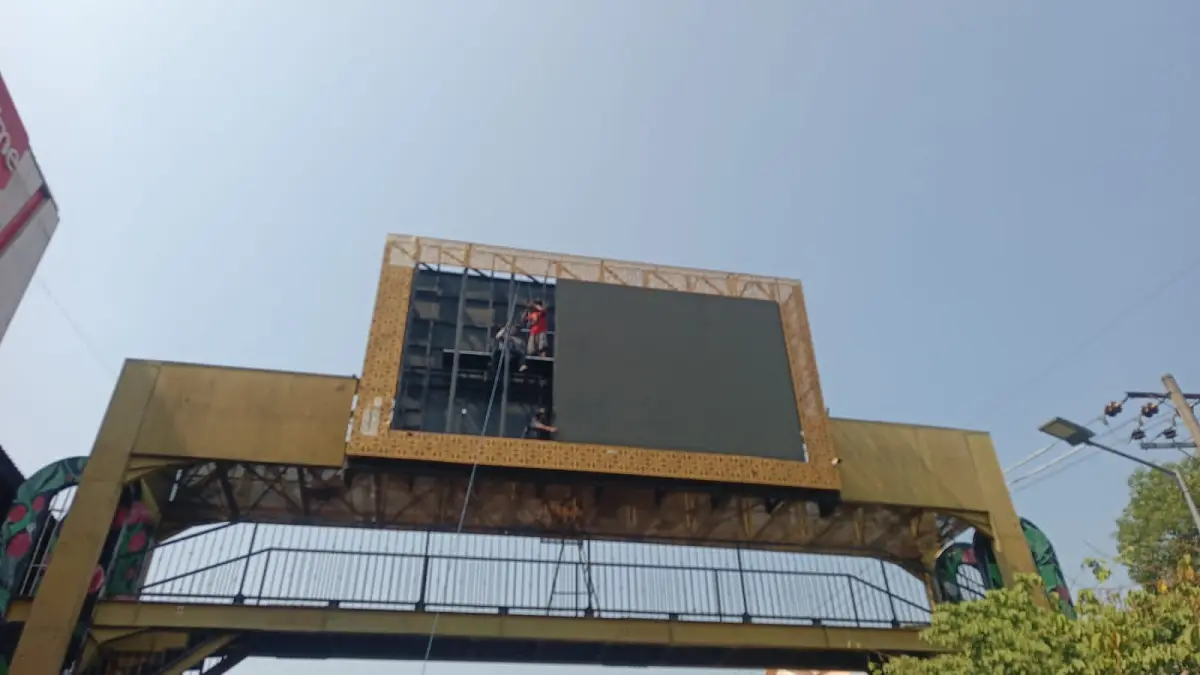 PENURUNAN ASSET: Pekerja menurunkan perangkat videotron di Jembatan Penyeberangan Orang (JPO) Jalan Pahlawan, Madiun, sebagai tahap awal sebelum pembongkaran konstruksi jembatan dan revitalisasi trotoar sisi barat PSC.
Foto: Bagas Bimantara/Jawa Pos Radar Madiun