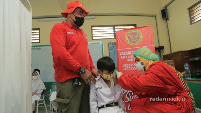 ALIHKAN PERHATIAN: Perwakilan Binda Jatim mendampingi anak-anak di MI Islamiyah 3 dengan hiburan agar tidak takut divaksin kemarin (29/12). (BAGAS BIMANTARA/JAWA POS RADAR MADIUN)