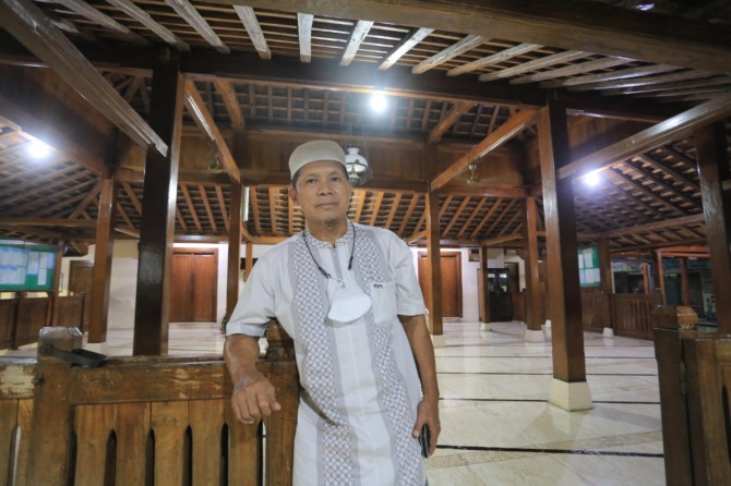 BERSEJARAH: Harminto berdiri dengan latar belakang bangunan masjid yang didominasi material kayu. (BAGAS BIMANTARA/JAWA POS RADAR MADIUN)