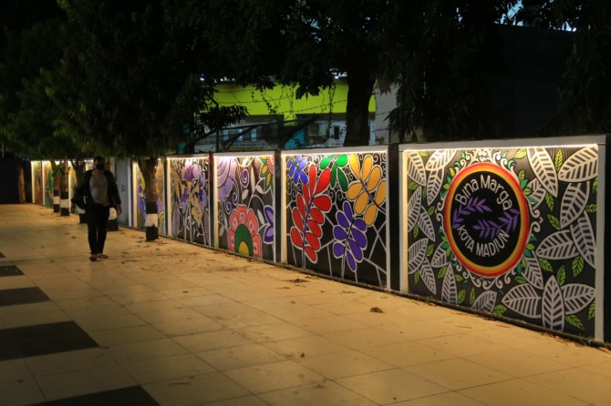 LEBIH CANTIK: Tembok di sepanjang Jalan Rimba Dharma dimural warna-warni dengan tema Madiun Kota Sejuta Bunga kemarin (14/8). DLH Kota Madiun berupaya mencegah vandalisme dengan memural tembok dan bangunan terbengkalai. (BAGAS BIMANTARA/JAWA POS RADAR MAD