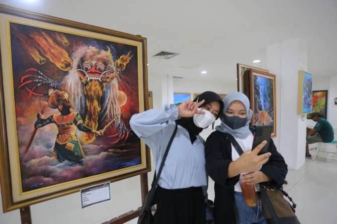 ARTISTIK: Dua remaja sedang berswafoto di dekat lukisan yang dipamerkan di Timbul Jaya Plaza. (BAGAS BIMANTARA/JAWA POS RADAR MADIUN)