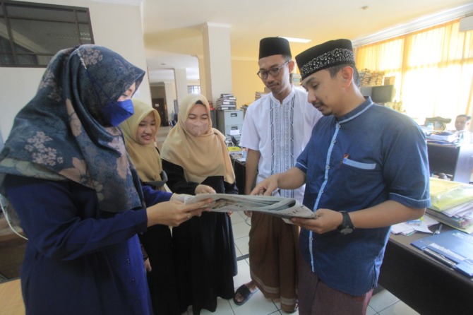 MOCO KORAN SARUNGAN: Pegawai pemkab meluangkan waktu membaca koran sebelum memulai aktivitas harian dengan mengenakan sarung dan pakaian musim di hari perdana kemarin. (AJI PUTRA/JAWA POS RADAR PONOROGO)