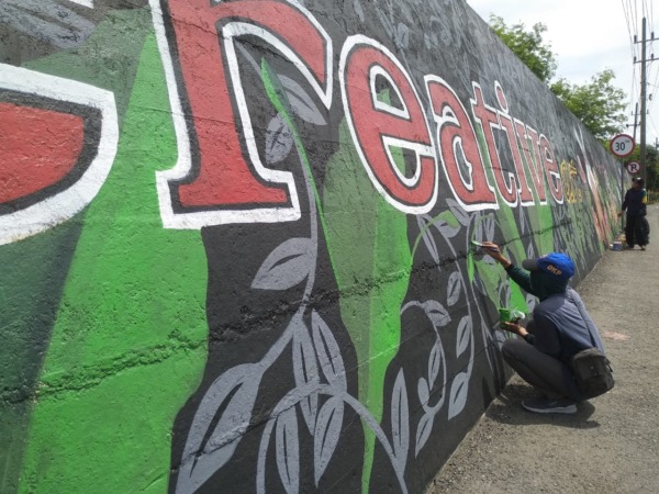 LEBIH ESTETIK: Tim kreatif DLH melukis mural di dinding bantaran Bengawan Madiun Jalan Ahmad Yani, Sabtu (12/11). (RAHMA DWI LESTARI/JAWA POS RADAR MADIUN)
