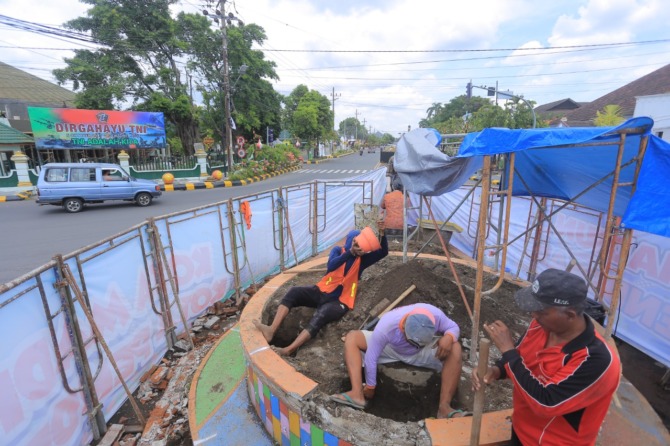 DIPERCANTIK: Sejumlah pekerja memugar patung penjual dan pembeli pecel di simpang empat Jalan Pahlawan kemarin (12/11). (BAGAS BIMANTARA/JAWA POS RADAR MADIUN)