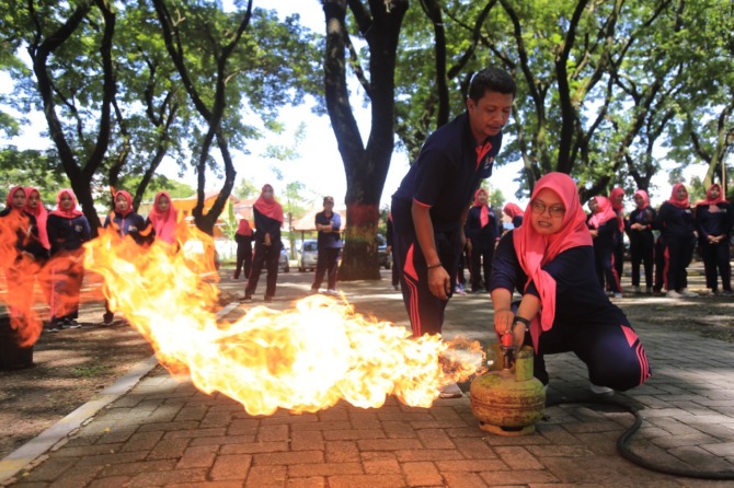 SIMULASI: Salah seorang warga dibantu petugas satpol PP dan damkar berupaya memadamkan api yang menyambar gas dari tabung elpiji kemarin. (BAGAS BIMANTARA/JAWA POS RADAR MADIUN)