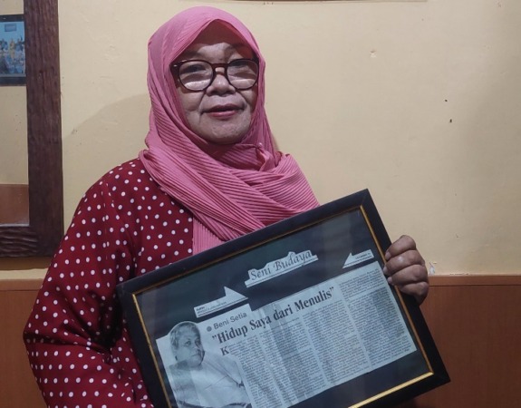BERDUKA: Sri Handayati menunjukkan salah satu karya tulis dan lukisan wajah mendiang Beni Setia, Minggu (25/12). (DIAN RAHAYU/JAWA POS RADAR MADIUN)