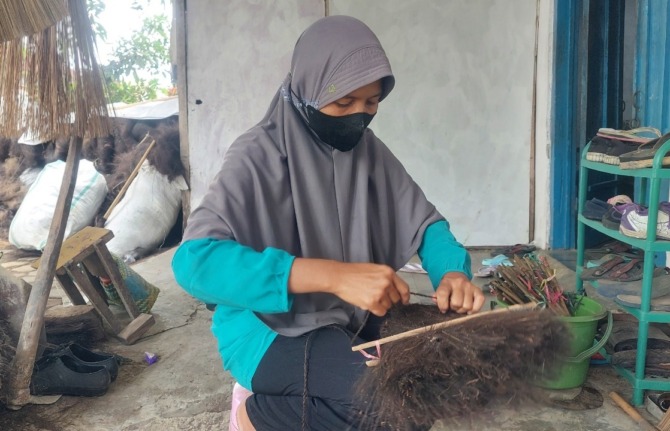 MANUAL: Istri Suryadi sedang menjahit sapu ijuk di rumahnya. (DIAN RAHAYU/JAWA POS RADAR MADIUN)