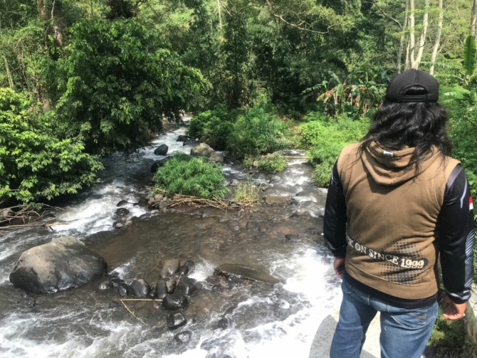 TERJEBAK BANJIR: Supri, warga Dusun Kandangan, Desa/Kecamatan Kare, terjebak banjir saat memancing di atas batu besar tengah sungai setempat, Kamis (23/3). (BAGUS RAHADI/JAWA POS RADAR MADIUN)
