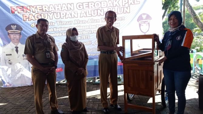 GEROBAK DORONG : Bupati Suprawoto didampingi Wabup Nanik Endang Rusminiarti dan Kadisperindag Sucipto menyerahkan gerobak baru kepada PKL di Alun-Alun Magetan. (ERIC WIBOWO/RADAR MAGETAN)
