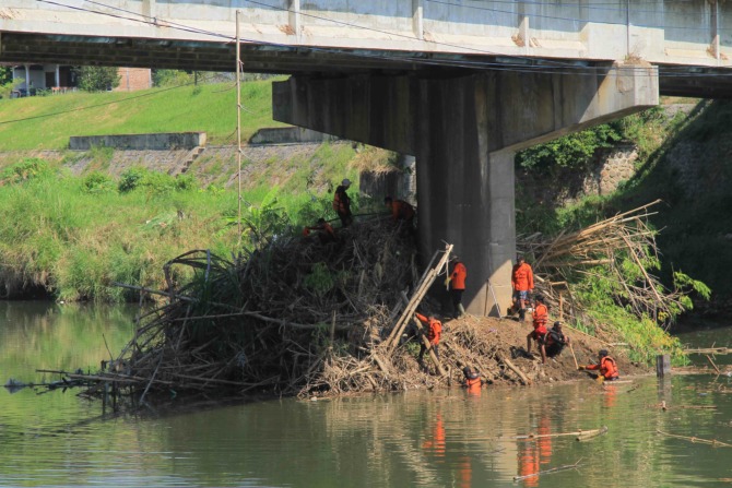 EVAKUASI: Puluhan petugas dan relawan BPBD Kota Madiun melakukan pembersihan sampah bambrongan yang nyangkut di tiang penyangga Jembatan Manguharjo kemarin (30/5). (BAGAS BIMANTARA/JAWA POS RADAR MADIUN)